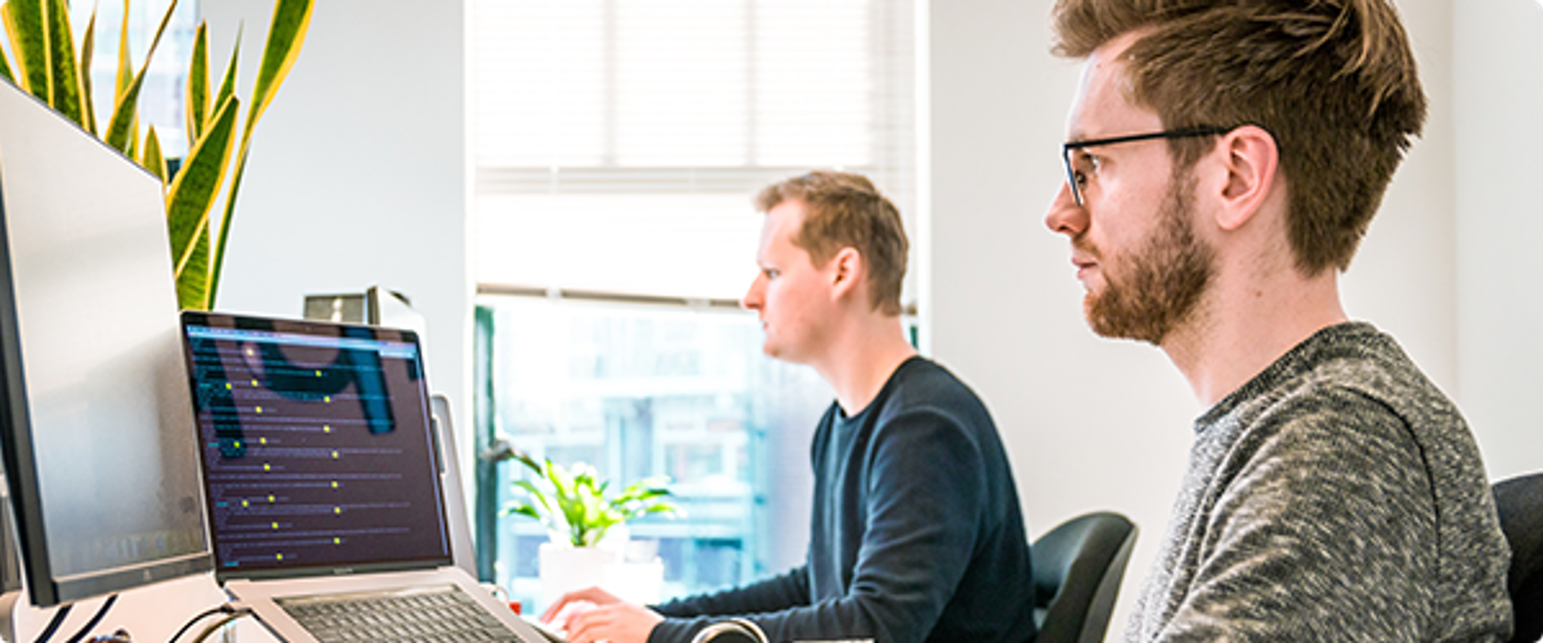 Two men sitting at a table working on their computers in a work setting.