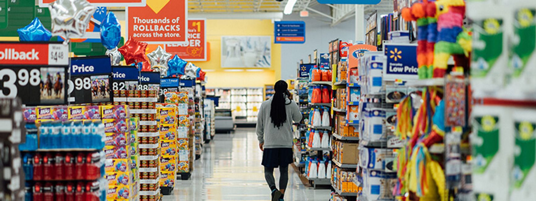 A photo of a woman walking through the colorful and chaotic aisles of a Walmart.