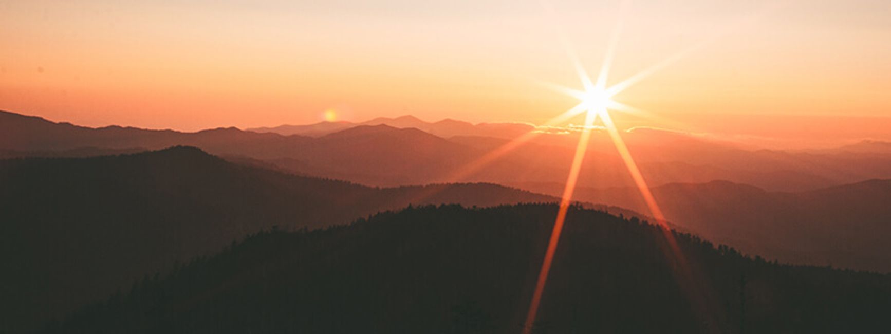 A photo of a sunrise over foresty mountains.