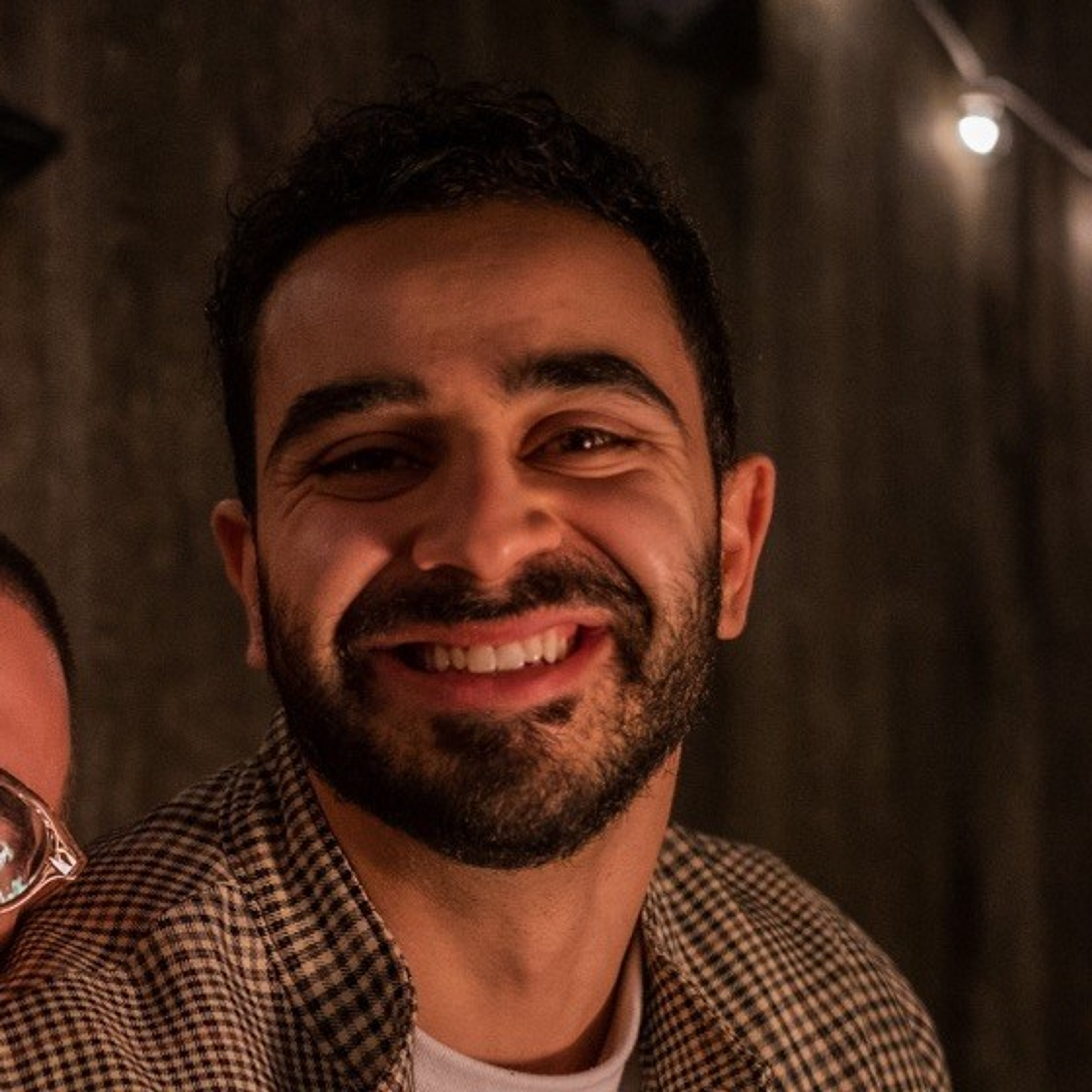 A smiling man with a beard, dark hair, and a plaid shirt.
