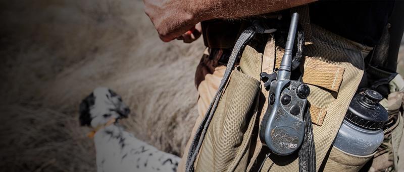 Weathered remote clipped to hunters gear bag with dog in background