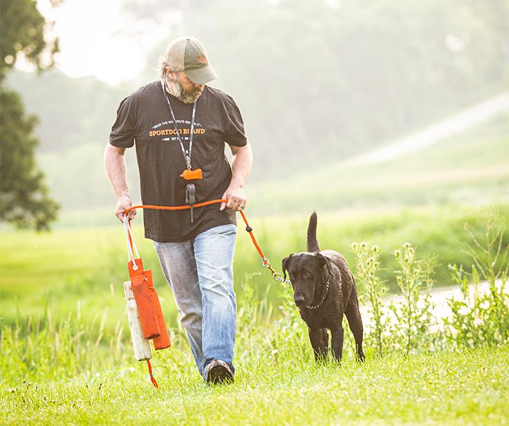 man walking black lab at heel while holding leash and canvas bumpers