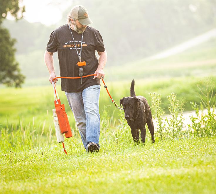 man walking with black lab on leash while hold training dummies