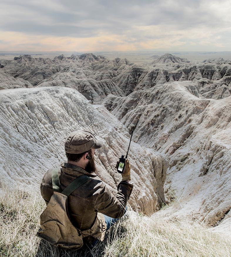 man sitting on ground looking at TEK handheld screen. Vast land in front of him