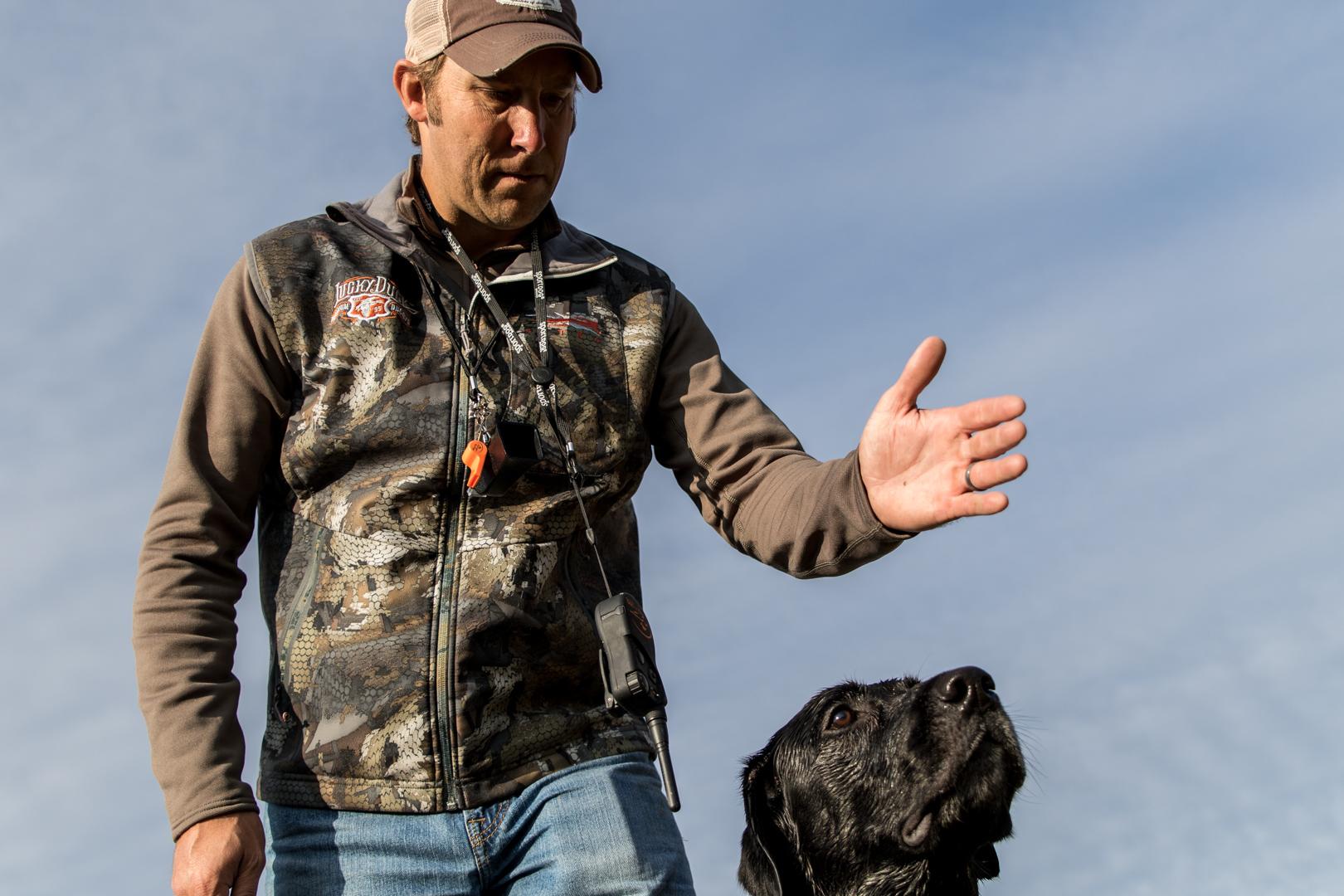 Man giving hand signal to black Labrador Retriever to go retrieve item.