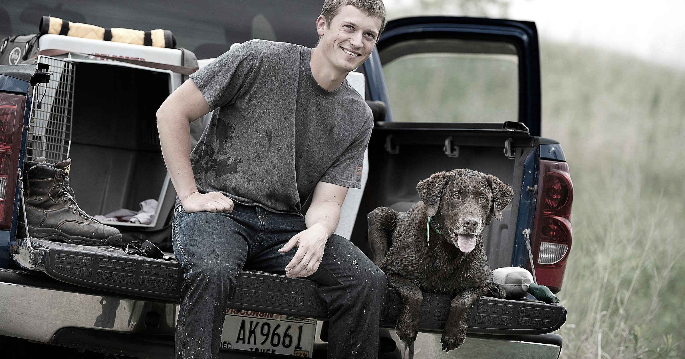Man and chocolate lab sitting on tailgate of truck