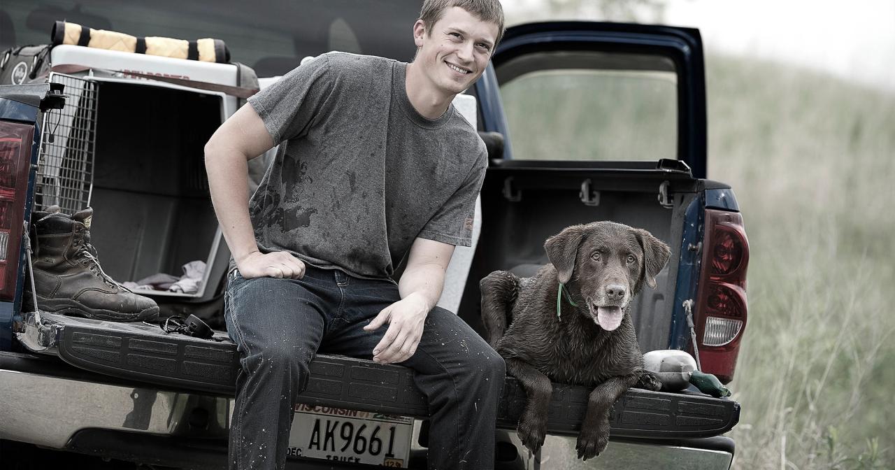 Josh Miller and his chocolate lab Easton sitting on tailgate of truck