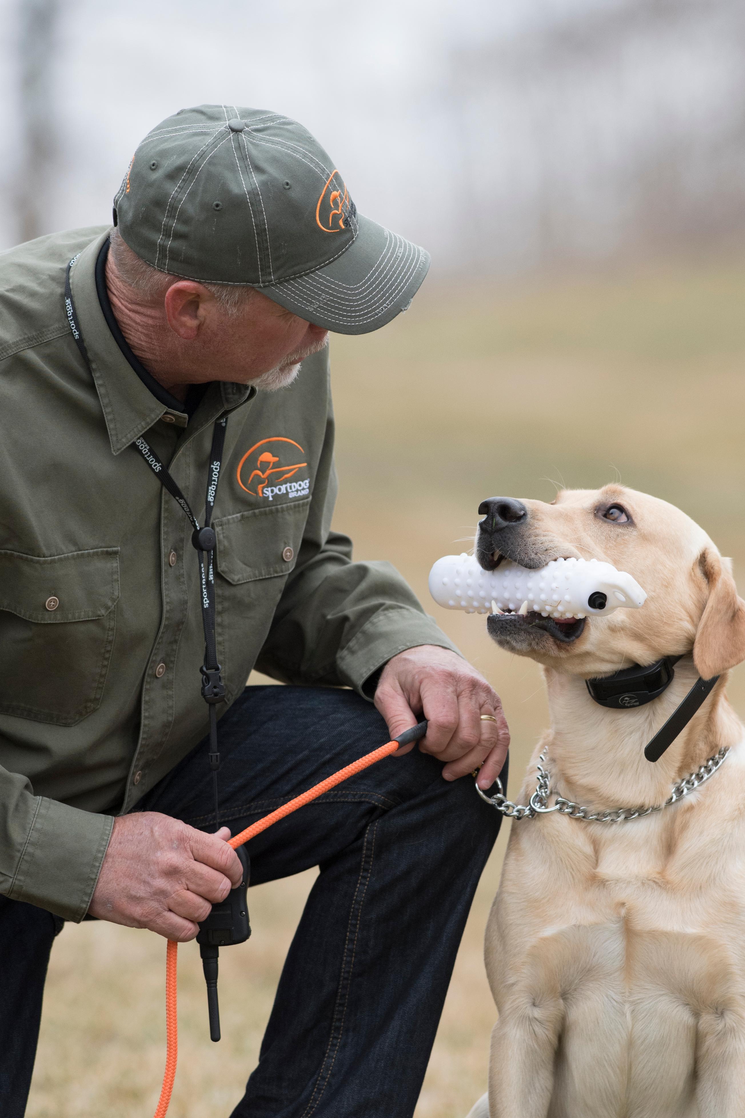 Charlie Jurney kneeling by yellow lab holding white plastic dummy