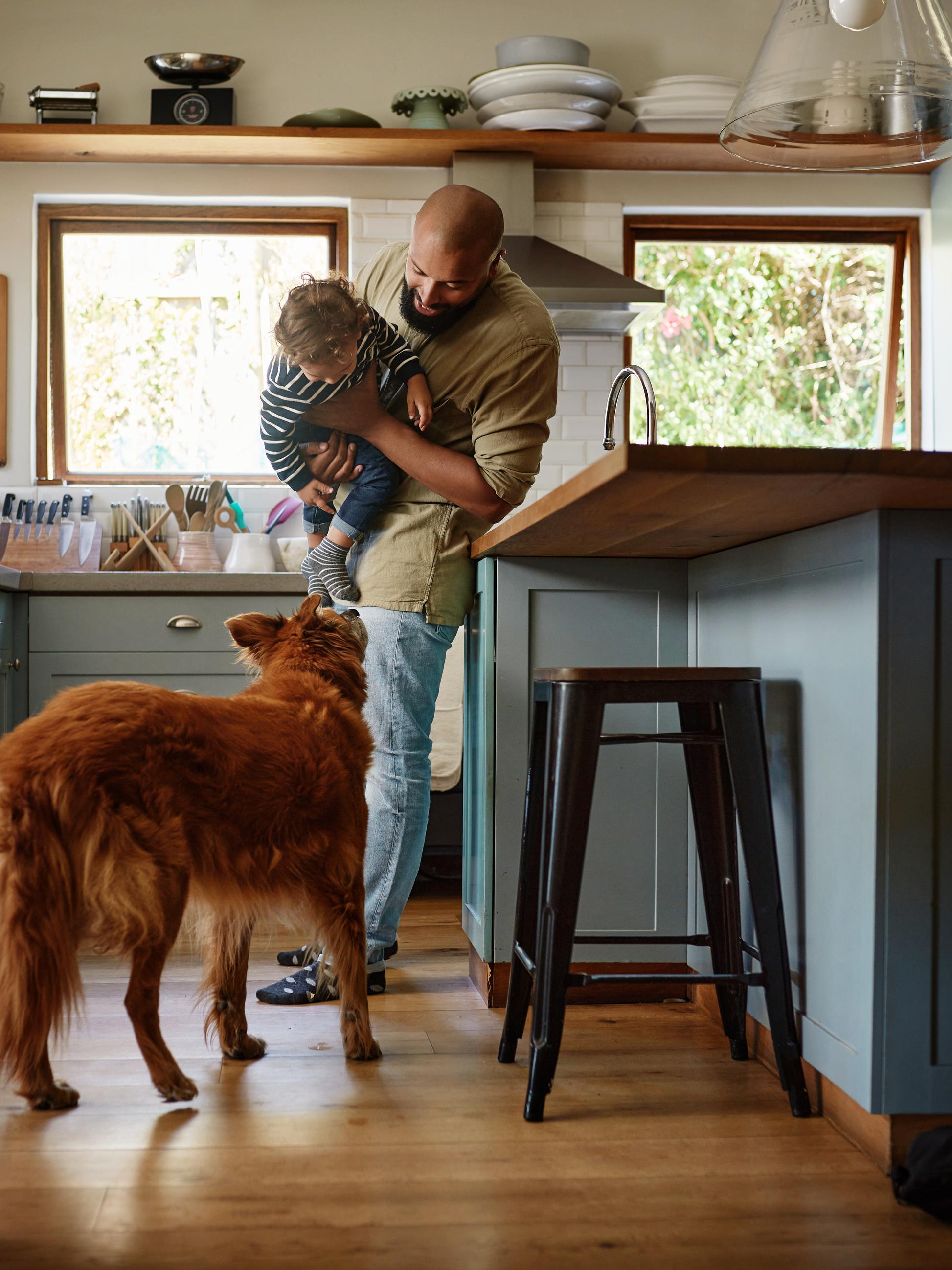 man plays with his son and dog in the kitchen
