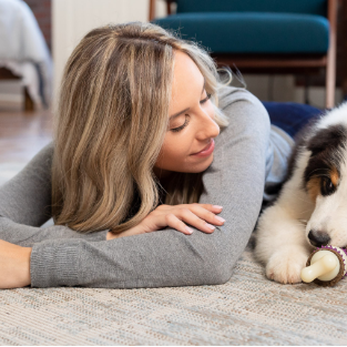 Woman laying in floor next to Aussie puppy