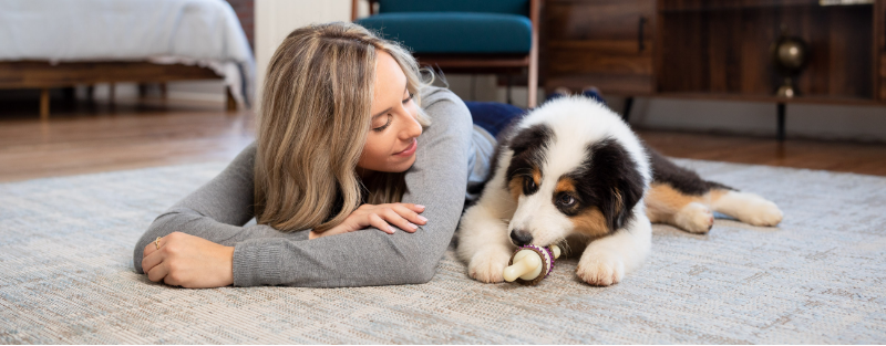Woman laying in floor next to Aussie puppy