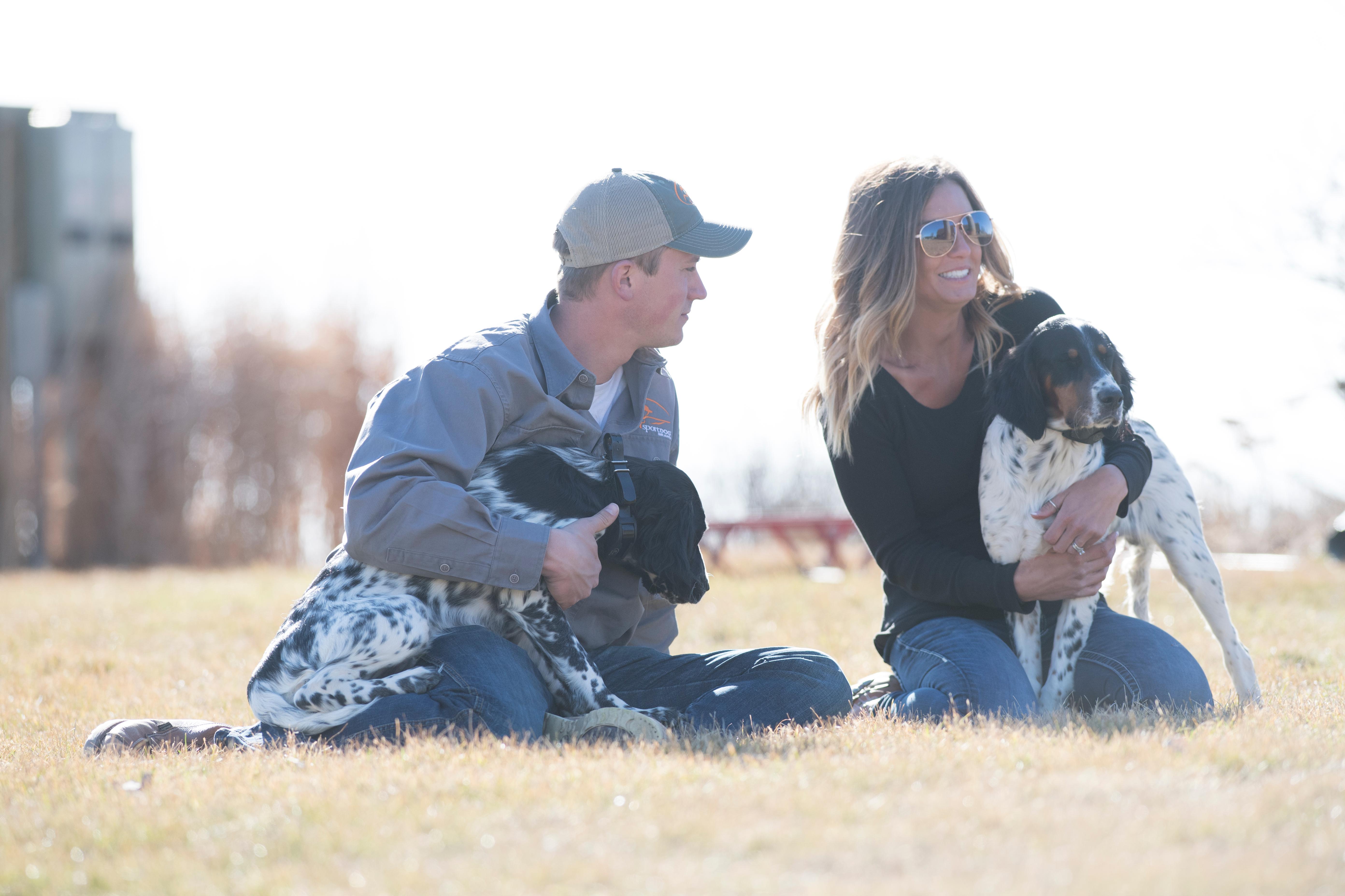 Man and woman sitting in grass with two setter puppies.