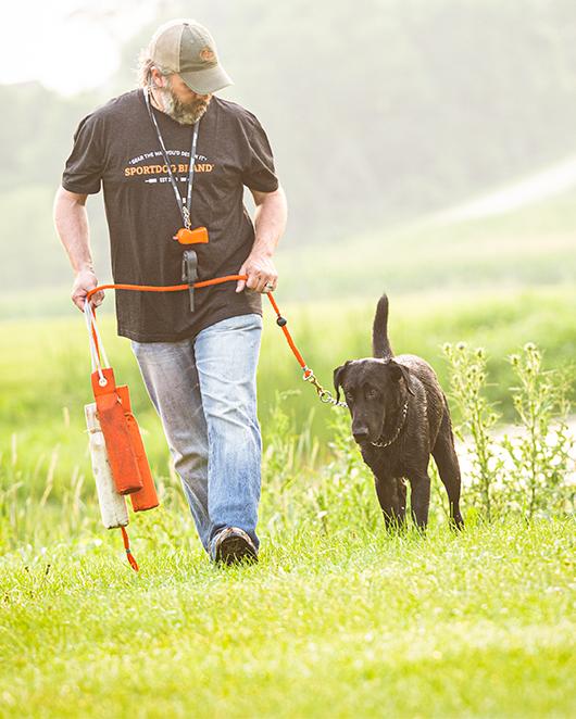 man walking with black lab on leash while hold training dummies