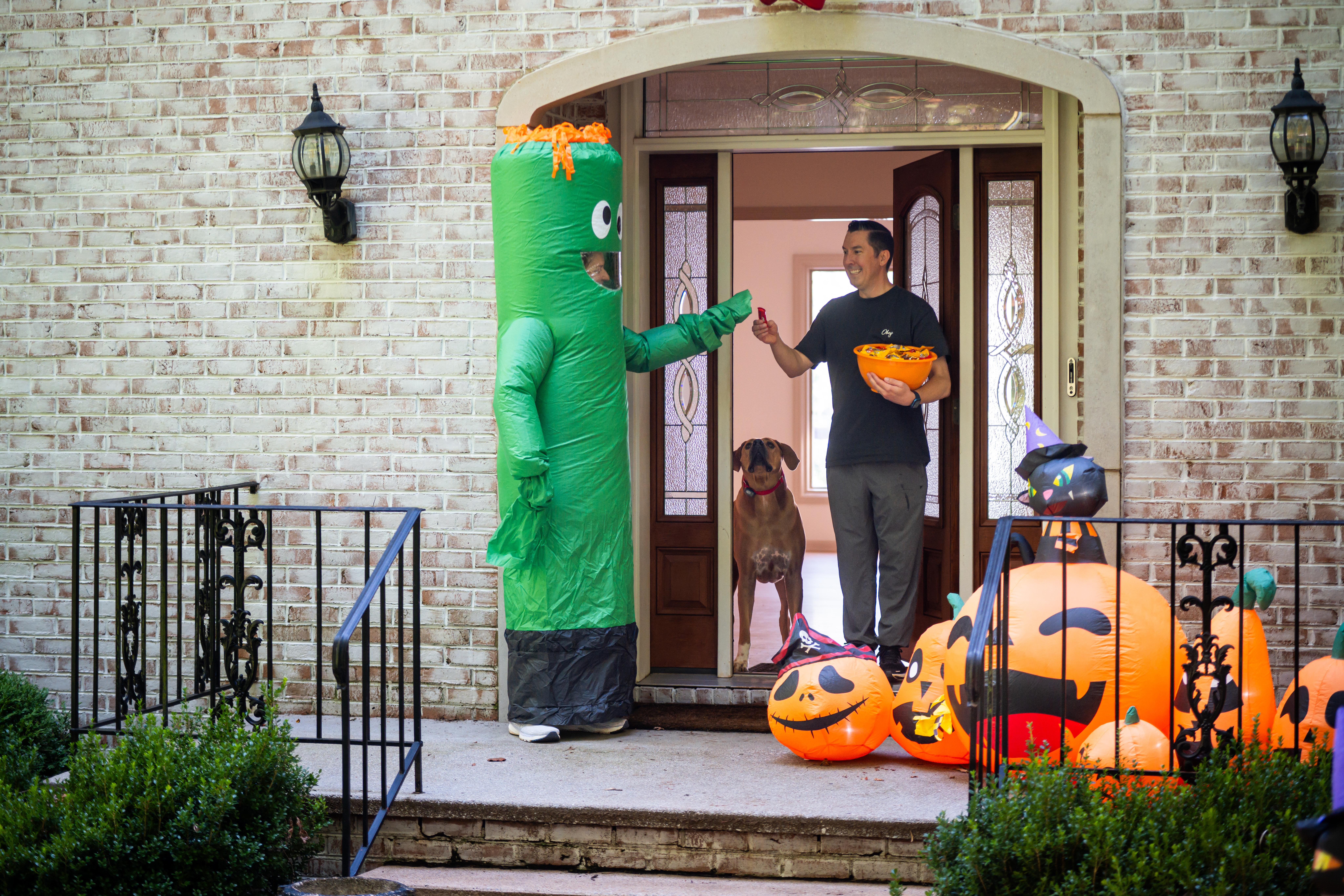 Trick or treater getting candy from homeowner with dog staying safely inside the door.