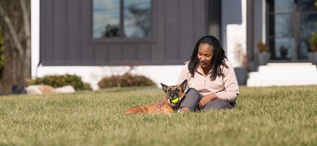 Woman sitting in front yard, petting Belgian Malinois dog