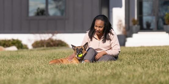 Woman sitting in front yard, petting Belgian Malinois dog