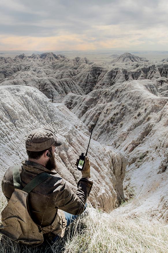 man sitting on ground looking at TEK handheld screen. Vast land in front of him