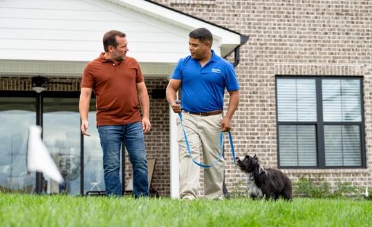 Invisible Fence trainer working with a black and white puppy in a yard with an invisible fence