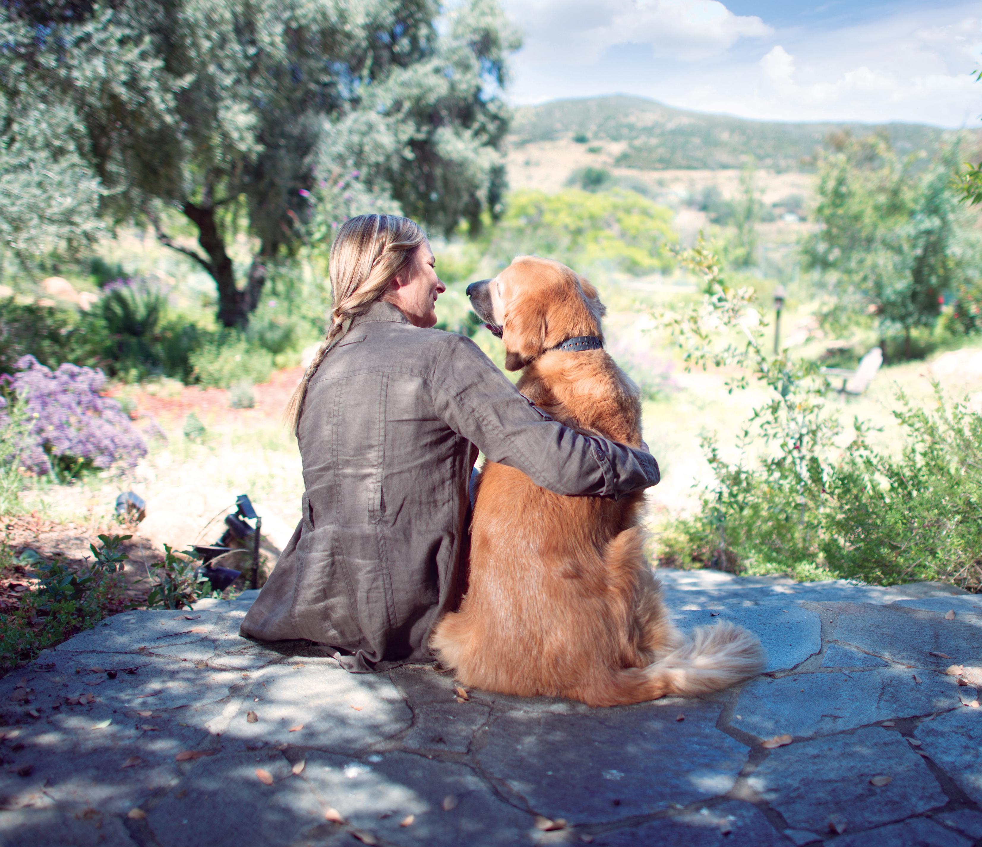 woman sits looking out over farm land with golden retriever wearing invisible fence gps dog collar