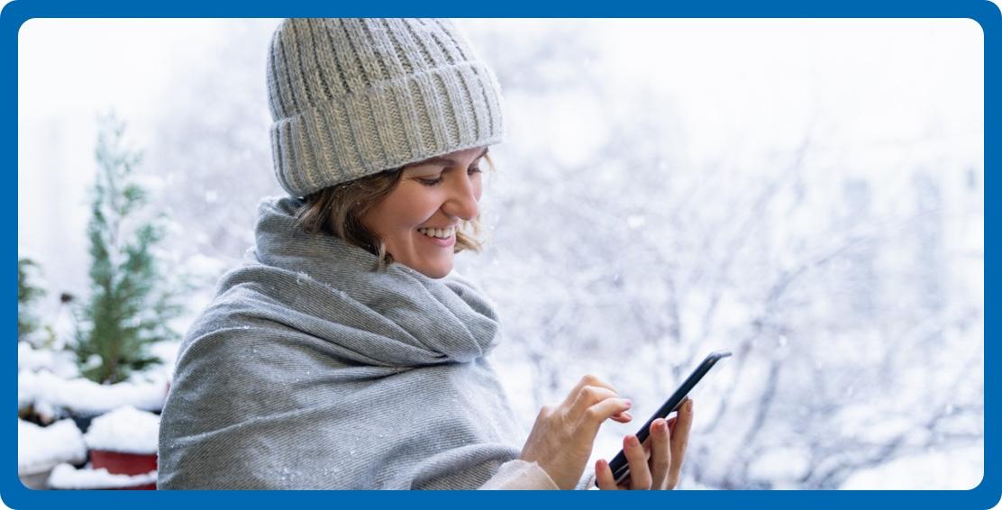Woman outside smiling while looking at phone
