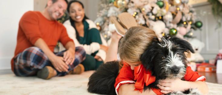Young girl hugging new puppy with mom and dad smiling in background