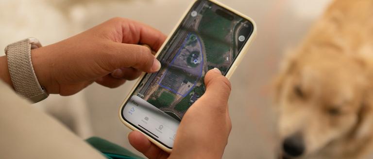 Person holding an iPhone with a GPS wireless dog fence map on screen and golden retriever in the background