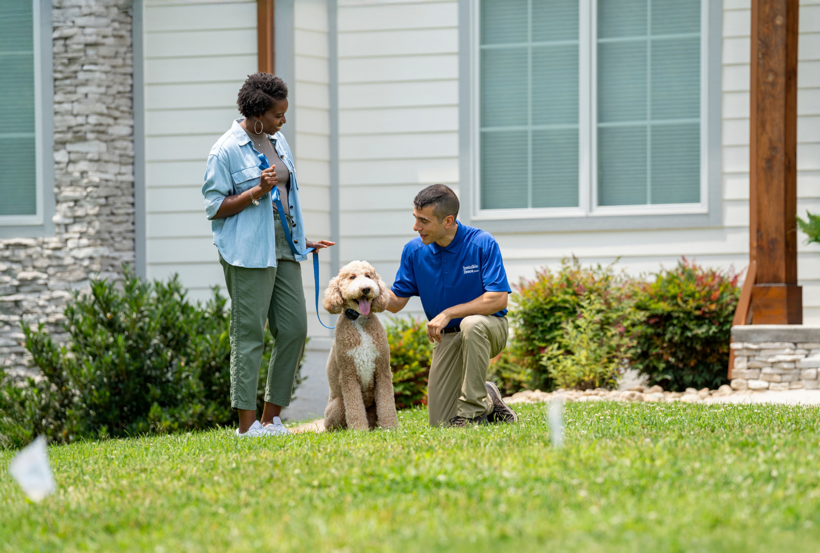 Goldendoodle on a held leash sitting in grass behind the Invisible Fence flags and with an Invisible Fence Brand trainer petting it