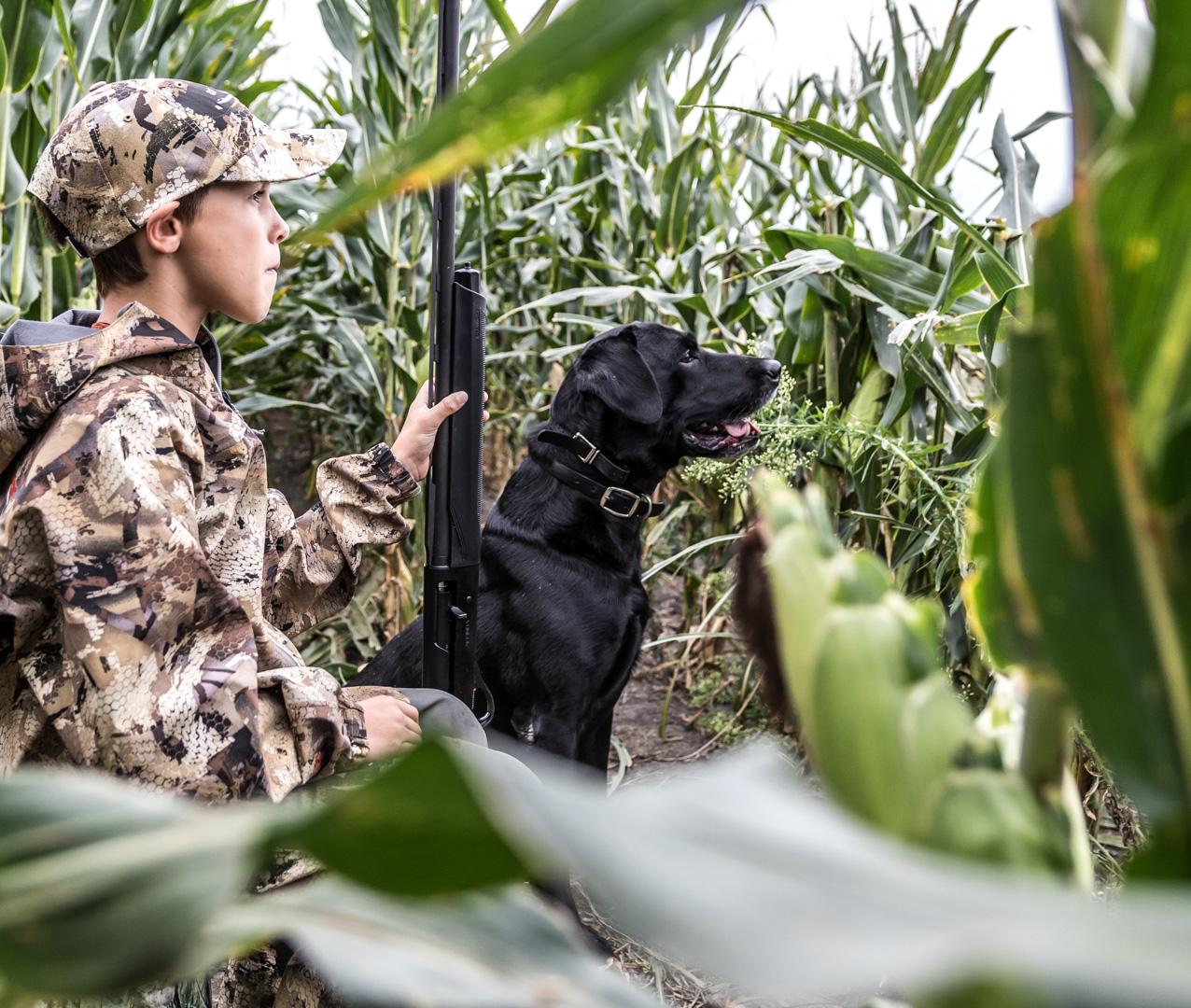 Young boy sitting with black lab. Both looking to sky for ducks.