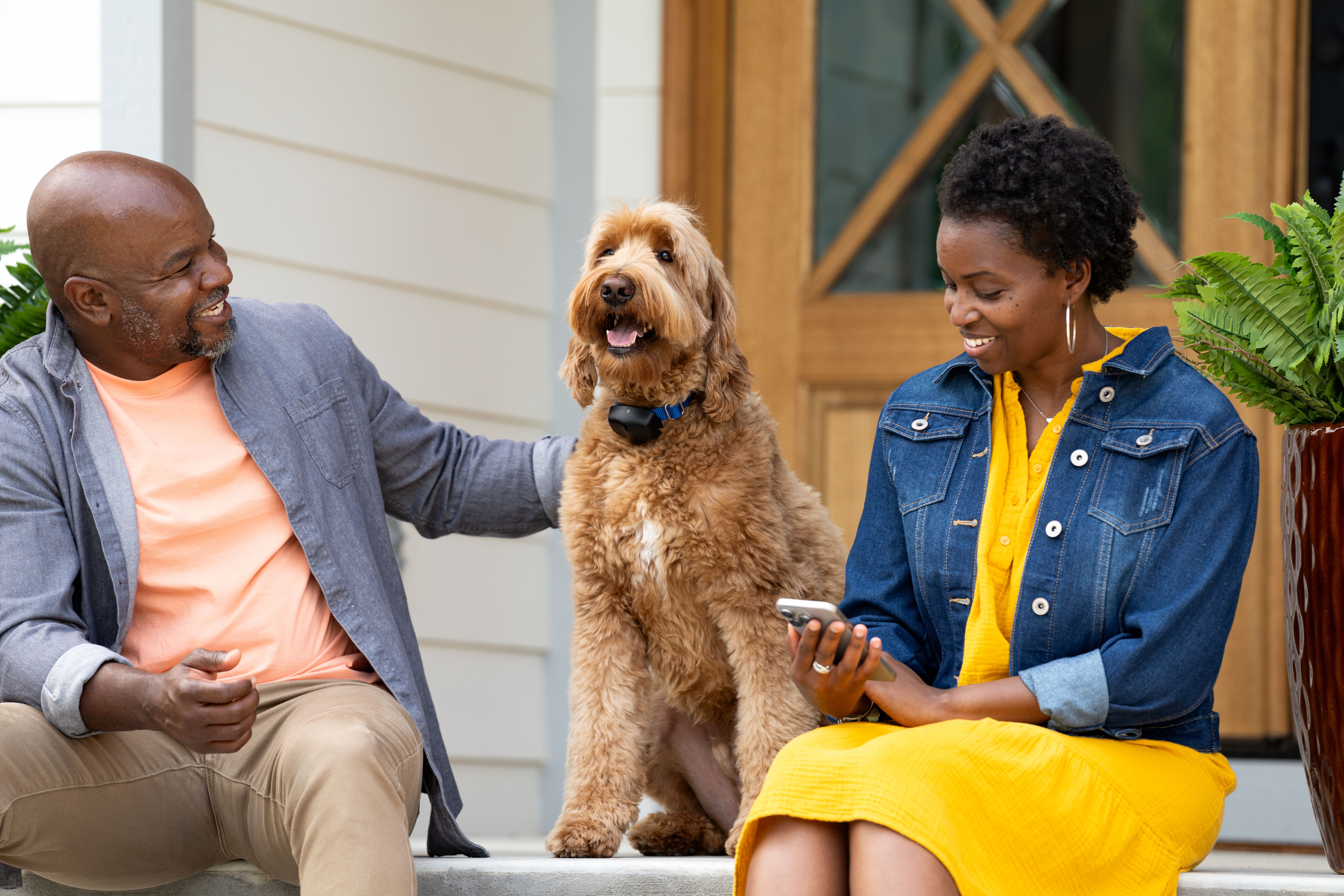 Woman sits on the porch with her husband and dog while checking her phone