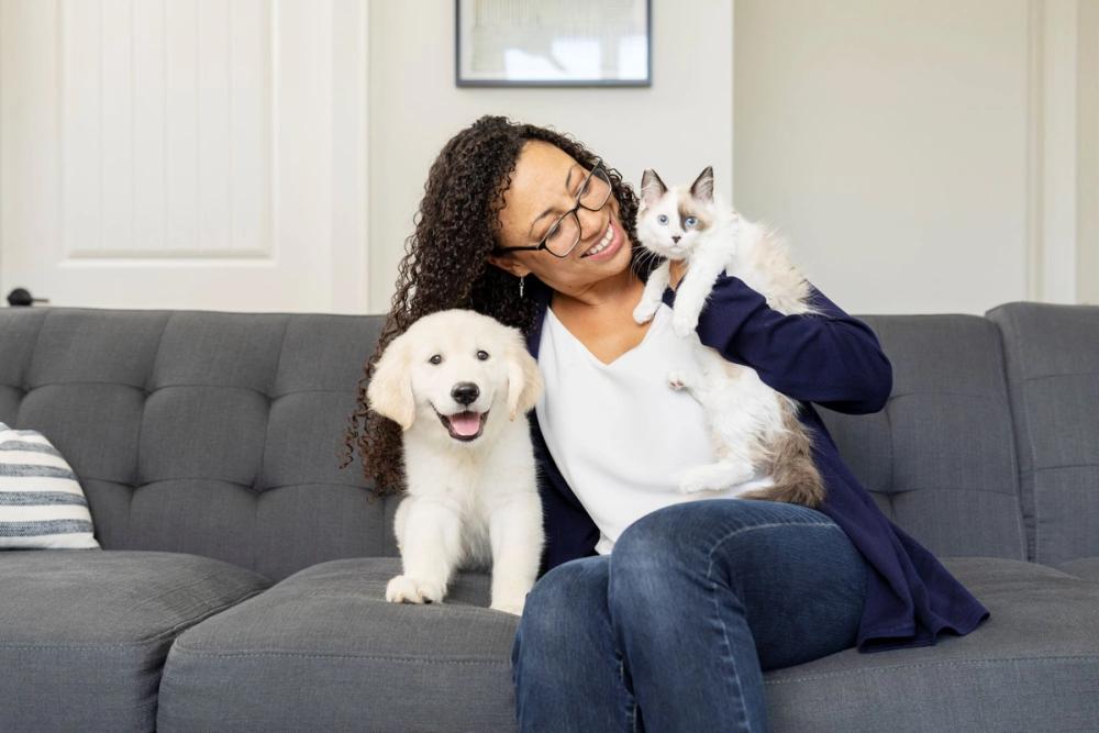 Woman holding puppy and kitten on couch