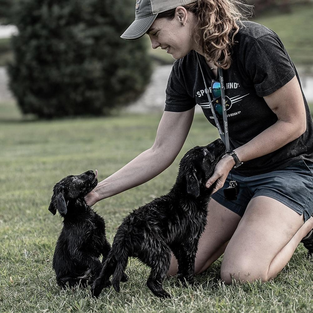 Woman smiling while petting two small black lab puppies