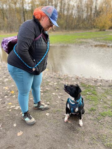 Jenny and Big Judy looking at eachother on a trail. Jenny is wearing a blue Kurgo hat and black winter jacket. Big Judy is wearing a blue Journey Air Harness.