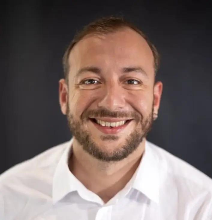 Umut Ozturk, Team Lead of Business Development for METYCLE; person wearing a white button down shirt in front of a black background, smiling and looking directly to the camera, with a beard and short brown hair