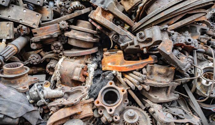 Pile of old, rusted metal parts, from machinery or vehicles. The parts include gears, pipes, brackets, and various other mechanical components, all showing significant signs of rust and wear. The metal surfaces are corroded, with many parts covered in a layer of orange-brown rust.