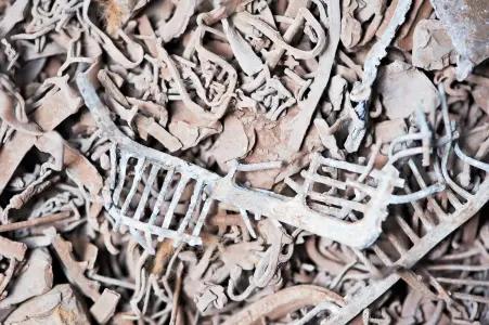 The image shows a tangled pile of rusty, weathered lead scrap. The pieces are remnants of various objects, with some recognizable shapes such as grates, rods, and other twisted or broken metal parts. The metal is heavily corroded, giving it a rough, textured appearance with a predominantly brown and orange color palette due to rust.