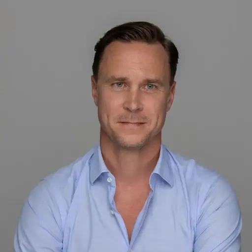 Veli Pekka Kiiski, Head of Business Development and Trading at METYCLE; person wearing a light blue button-down shirt in front of a dark grey background, slightly smiling, looking straight to the camera, with short dark wavy hair parted to the left