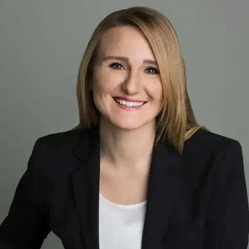 Irene Prinz, Head of People and Culture at METYCLE; person wearing a black blazer over a white shirt in front of a medium-gray background, smiling and looking directly at the camera, with long blond hair