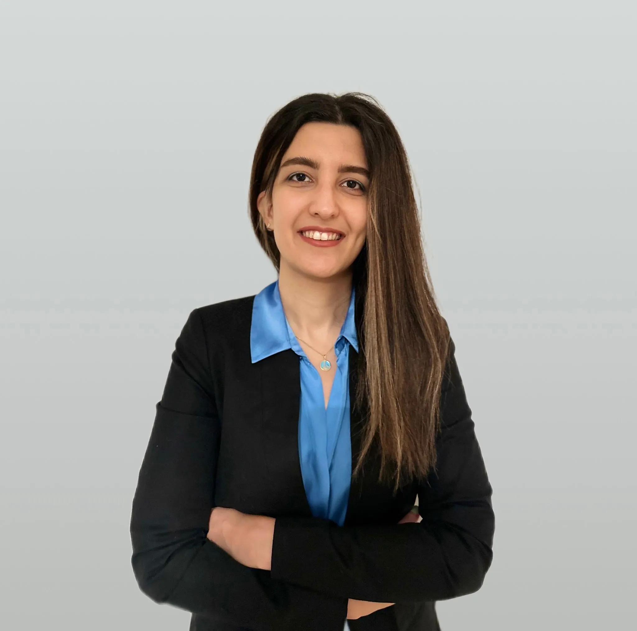 Parnian Seifi, Product Manager at METYCLE; person wearing a blue button down shirt, with a black blazer, standing in front of a light gray background, smiling directly to the camera, with long straight brown hair parted in the middle