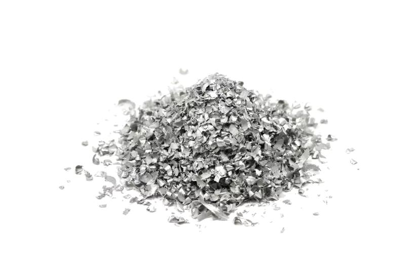 Small pile of shredded or finely broken magnesium. The pieces are irregular in shape, with jagged edges, and vary in size from tiny flakes to slightly larger fragments. The material is silver and reflective, giving it a shiny appearance. The pile is isolated on a plain, white background, making the metallic texture and the scattered nature of the fragments stand out.
