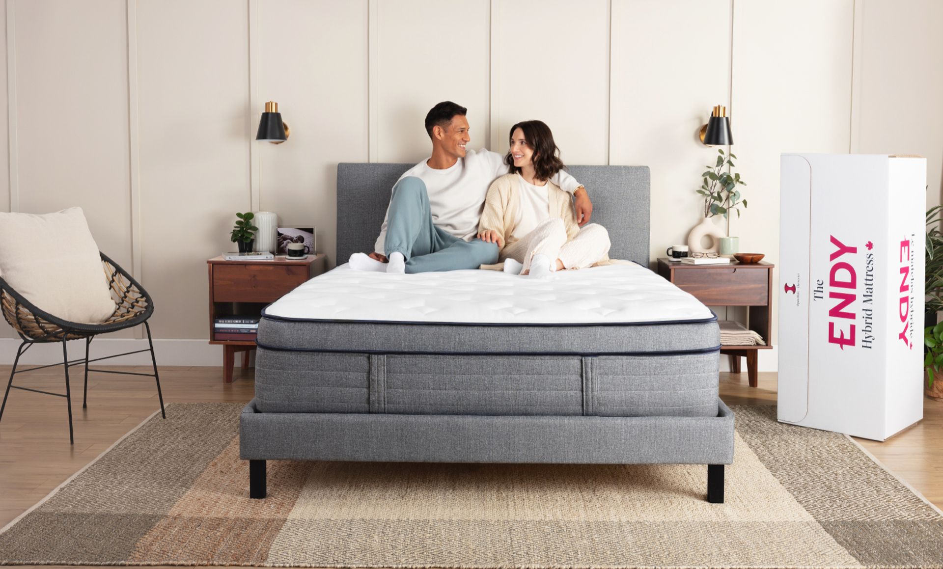 Man and woman sit on an Endy Hybrid mattress on a grey bed frame in a bedroom