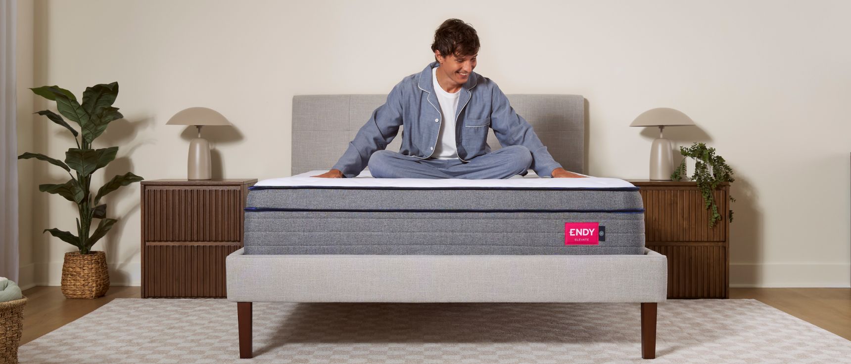 Man sitting cross-legged on an Endy Elevate Hybrid mattress on a white upholstered bedframe