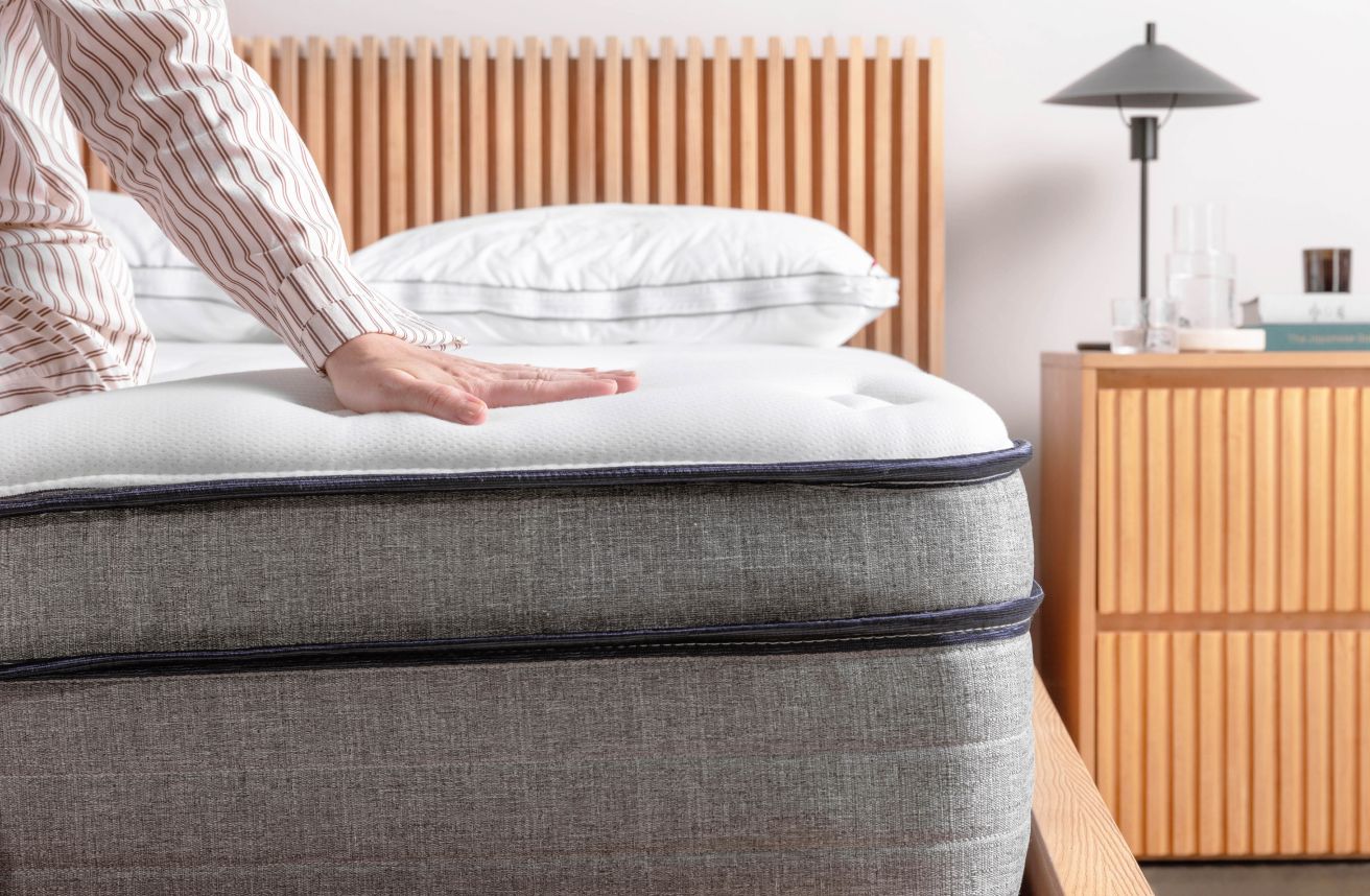 Person sitting on the edge of the Endy Hybrid Mattress to demonstrate construction.