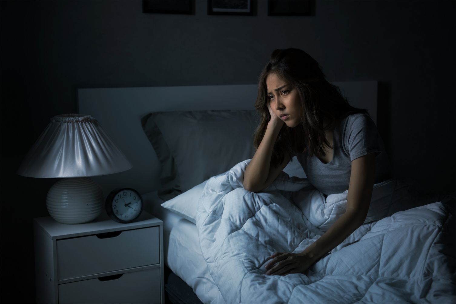 A person sitting down in bed looking frustrated and tired.