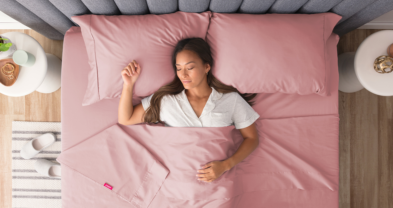 A woman sleeping in bed, dressed with the Endy Sheet Set in Cherry Blossom.