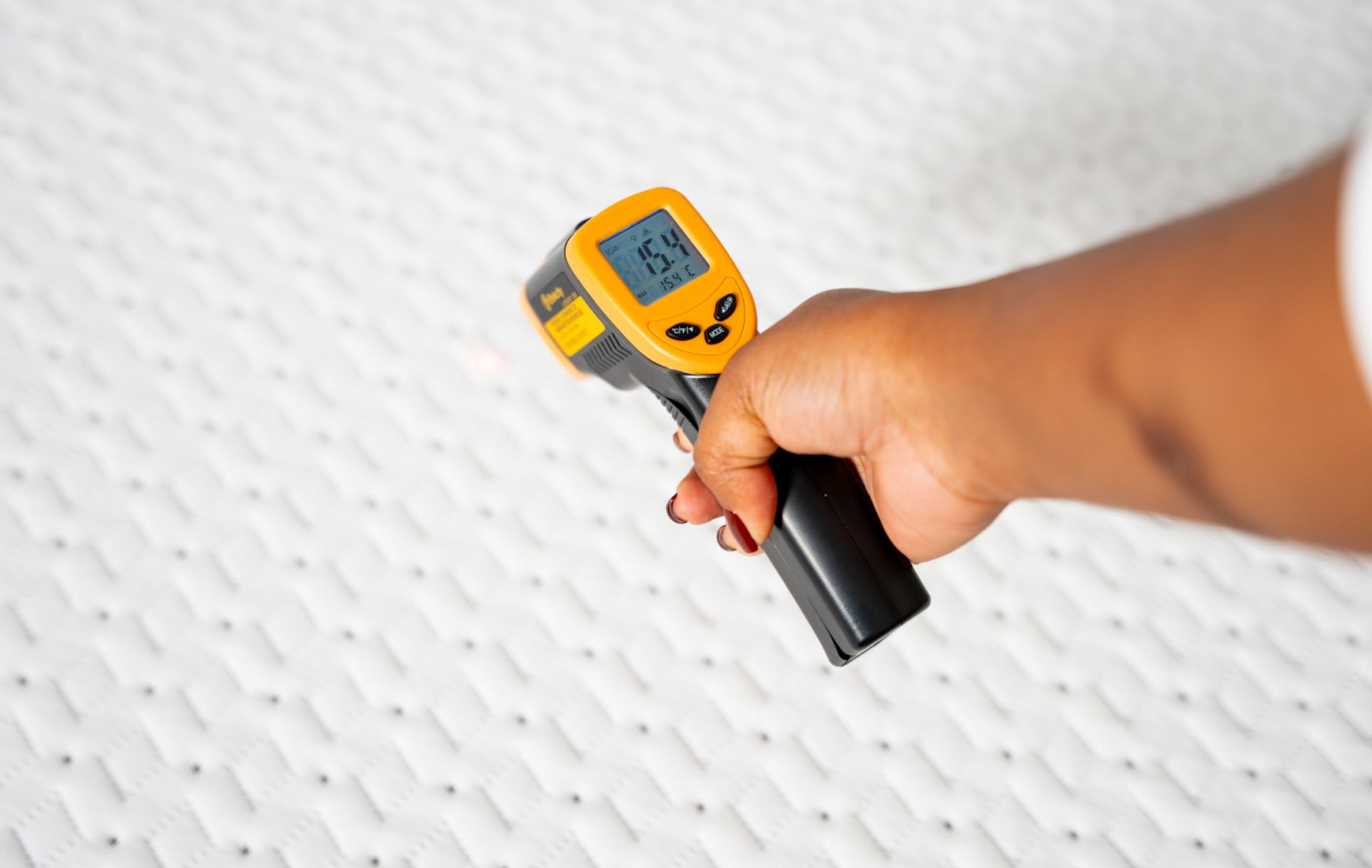 Close up of the surface of the Endy Mattress, a woman's arm reaches in with a heat gun to measure the temperature of the mattress