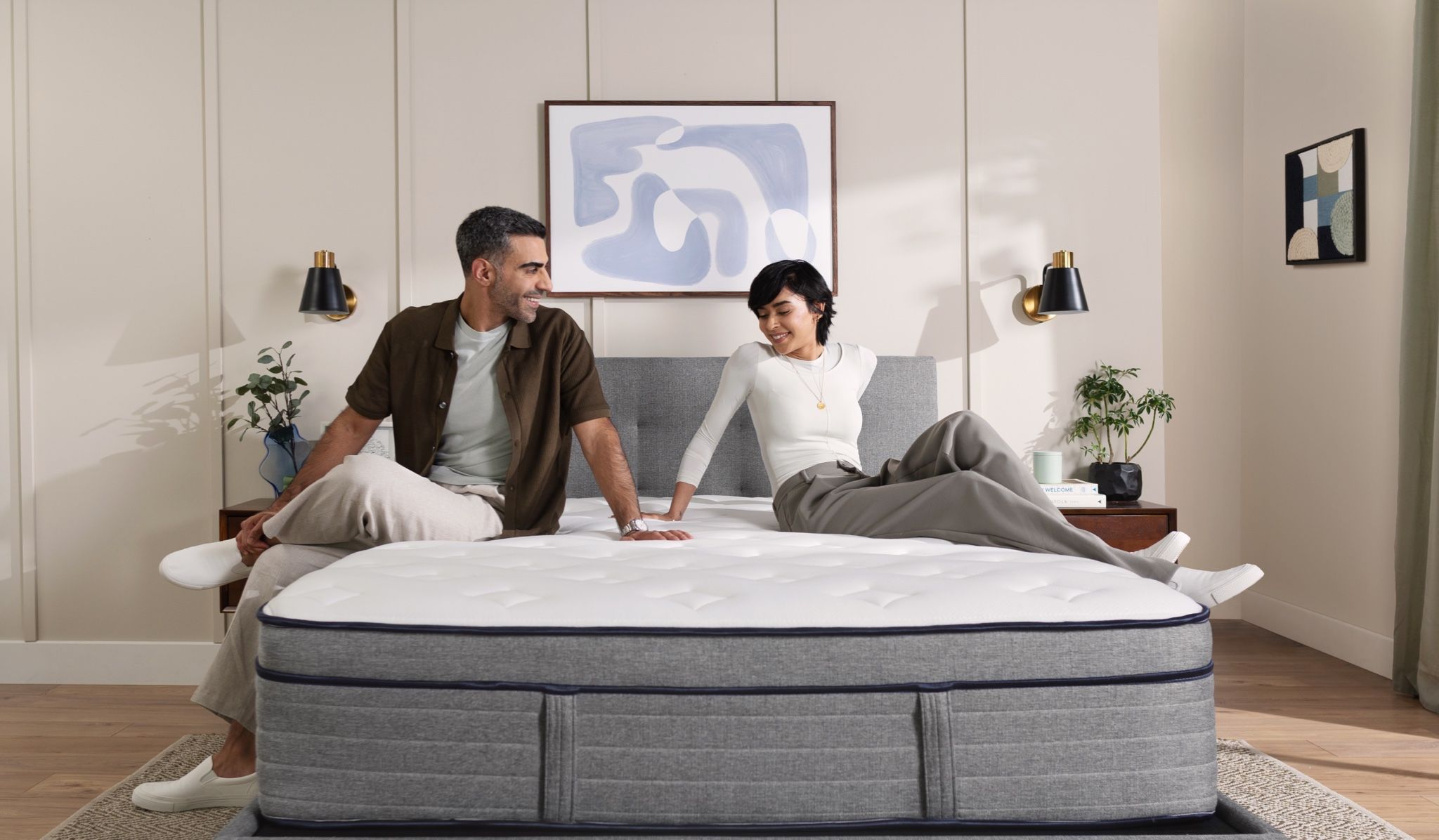 Man and woman sitting on a bare Endy Hybrid mattress in a beige room