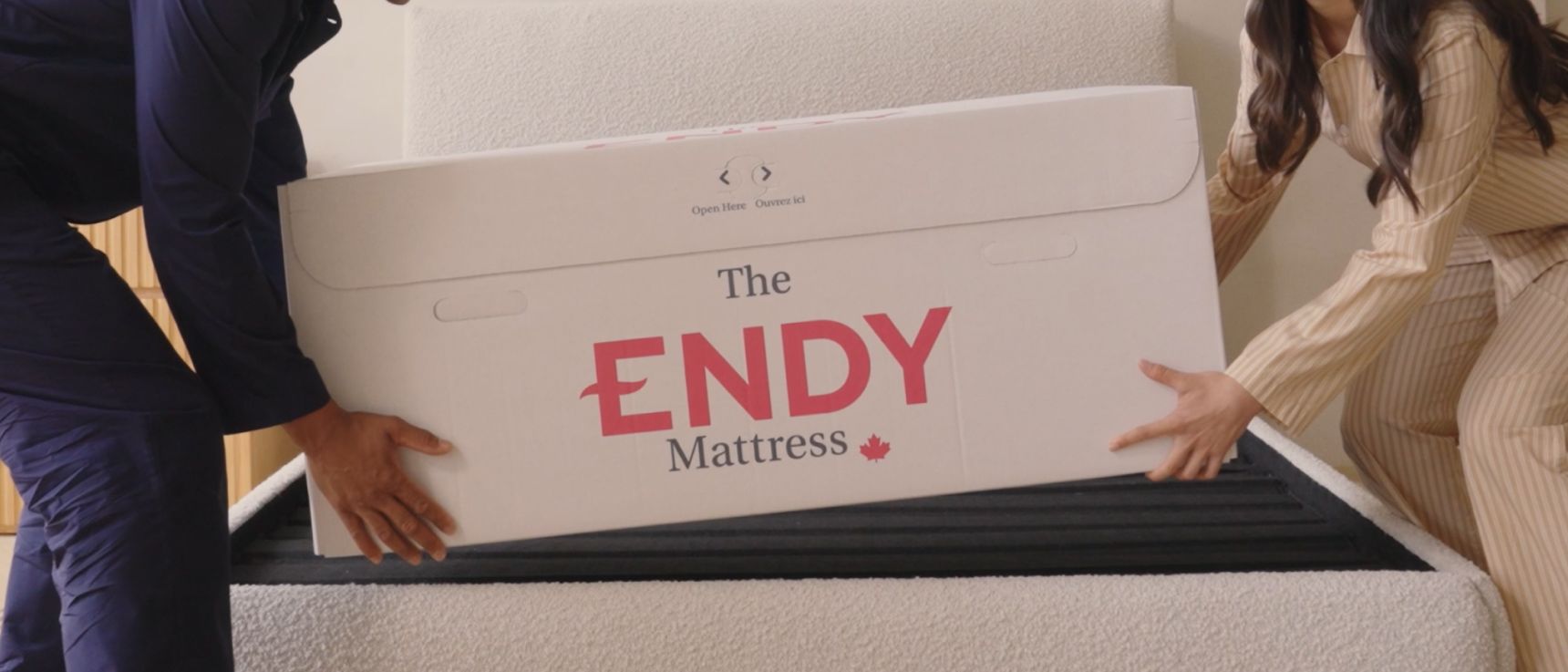 2 people wearing pyjamas place an Endy box onto a white upholstered Endy bed frame
