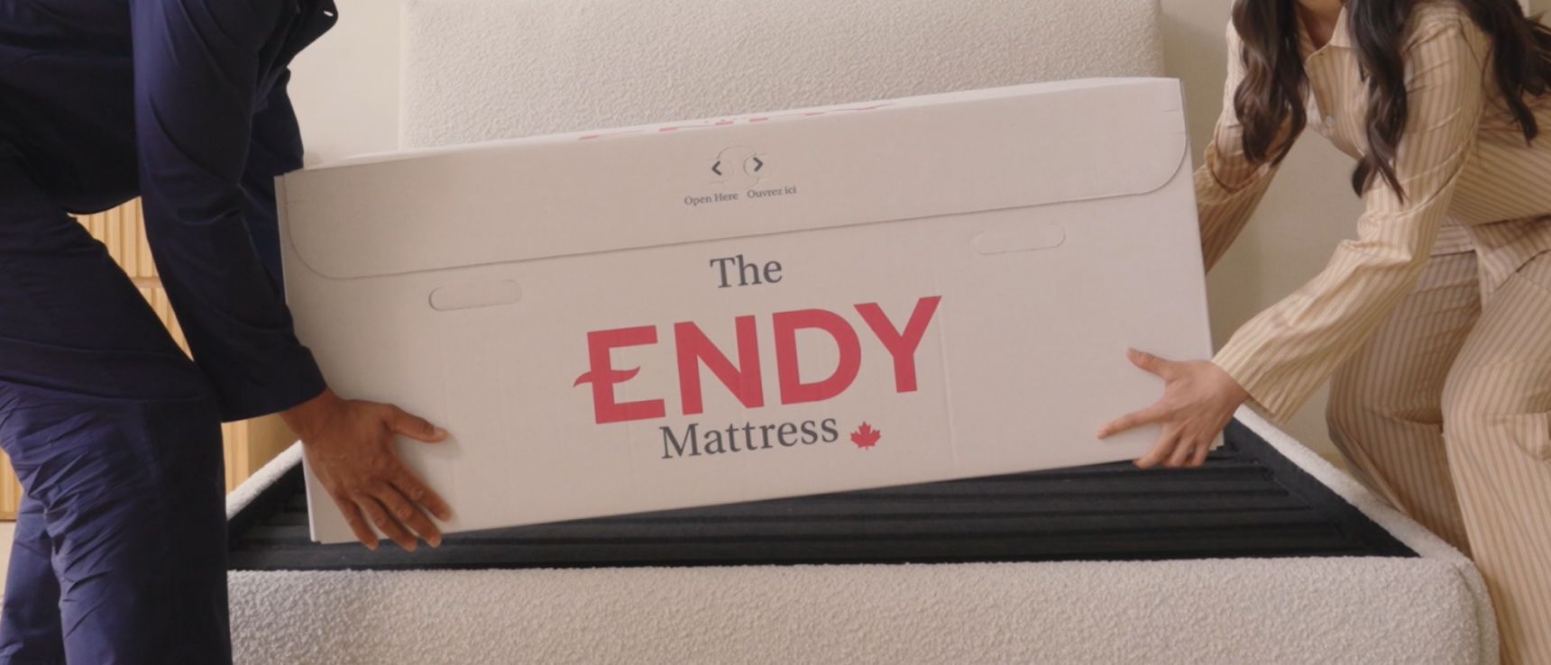 A man and woman in pajamas place an Endy mattress box onto an empty bed frame