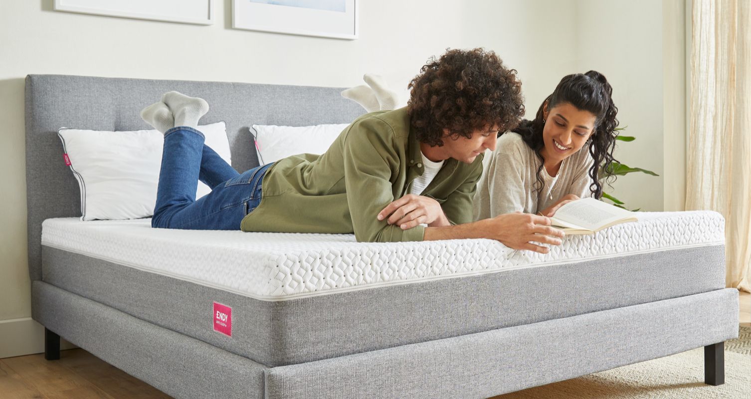 A couple lying down on their stomachs on an Endy Mattress, reading a book together