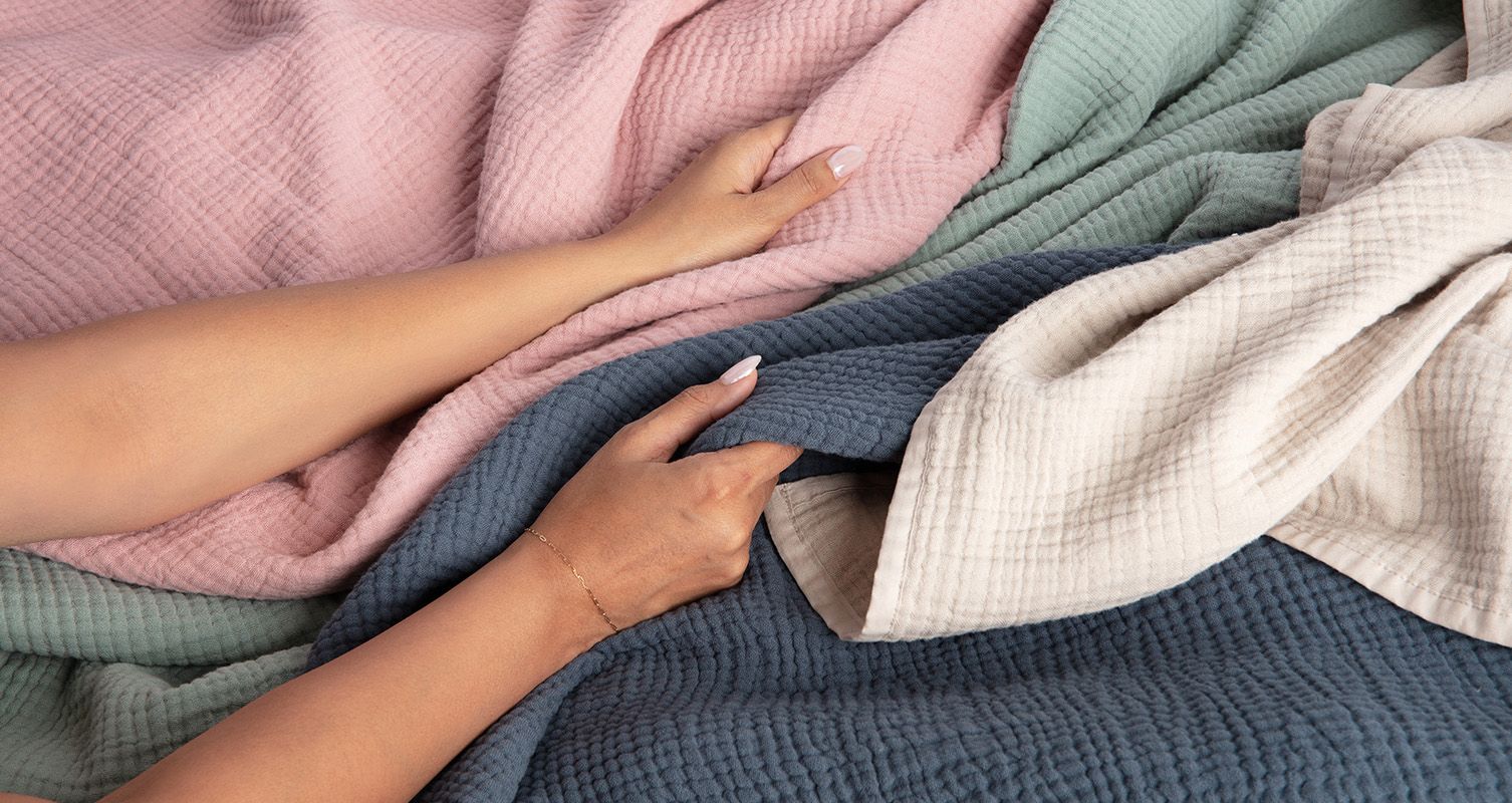 The Endy Muslin Blankets in Cherry Blossom, Soft Sage, Midnight Navy and Coastal Tan.